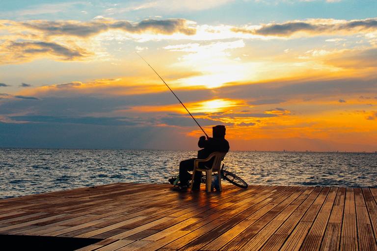 man fishing on a wooden deck during sunset